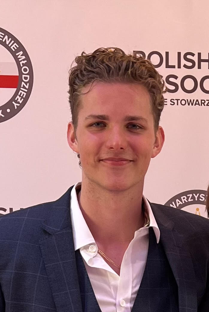 Person smiling in front of a Polish Modern Art Foundation backdrop, wearing a formal dark blazer over a white shirt.