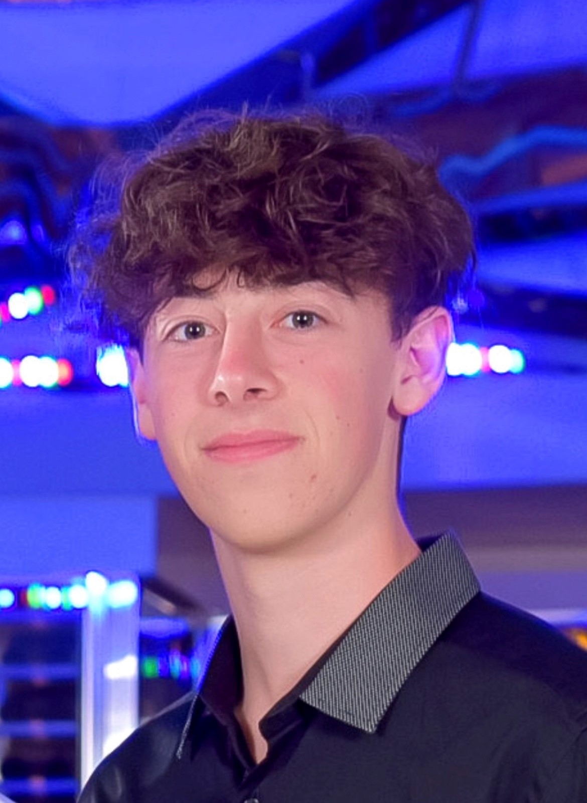 Person smiling, wearing a black shirt with a background of blurred colorful lights.