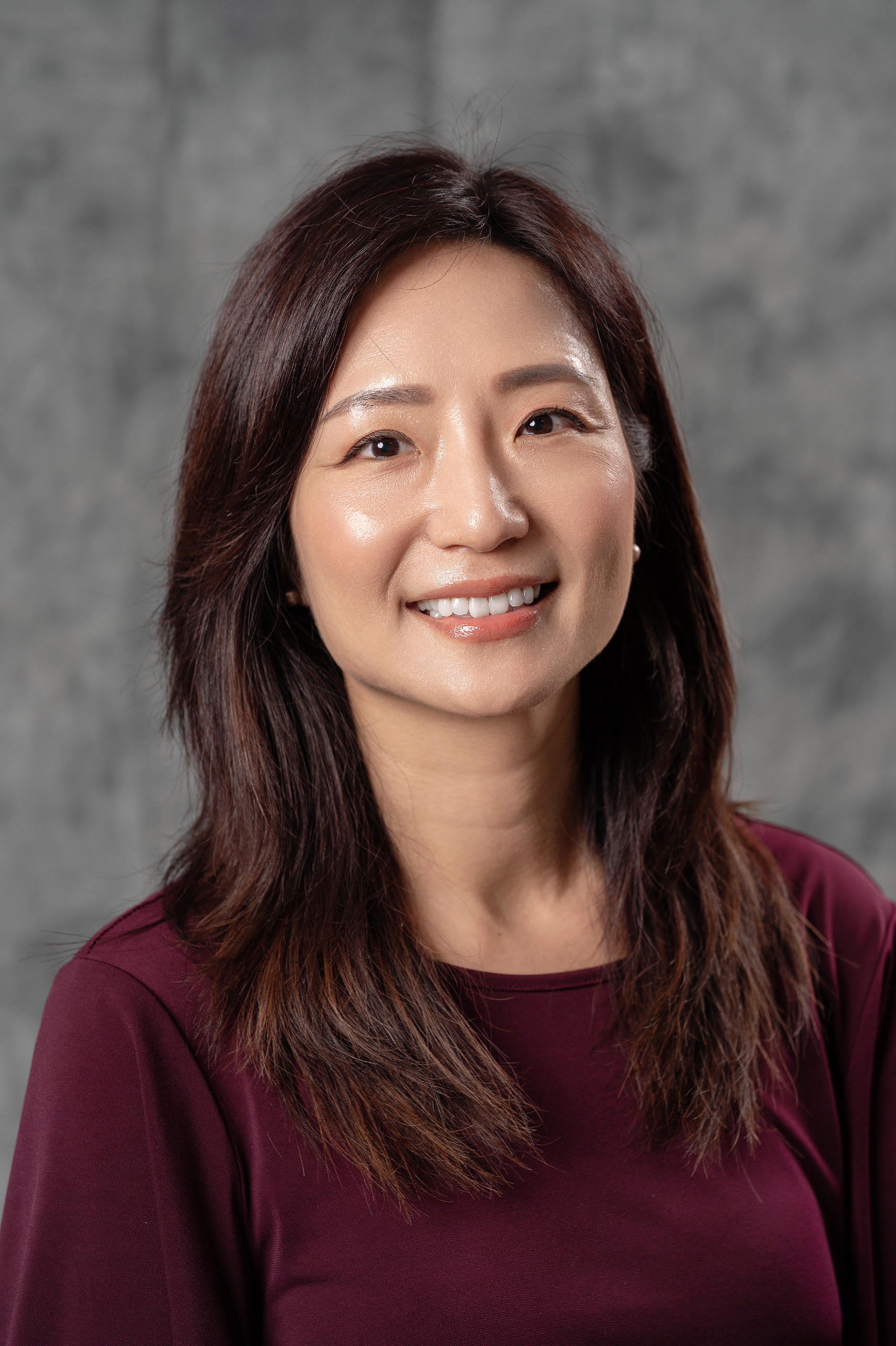 Ming Huang, with shoulder-length brown hair and a burgundy top, smiling