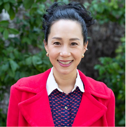 A smiling woman dressed in a red coat and blue shirt, showcasing a joyful expression and vibrant style.