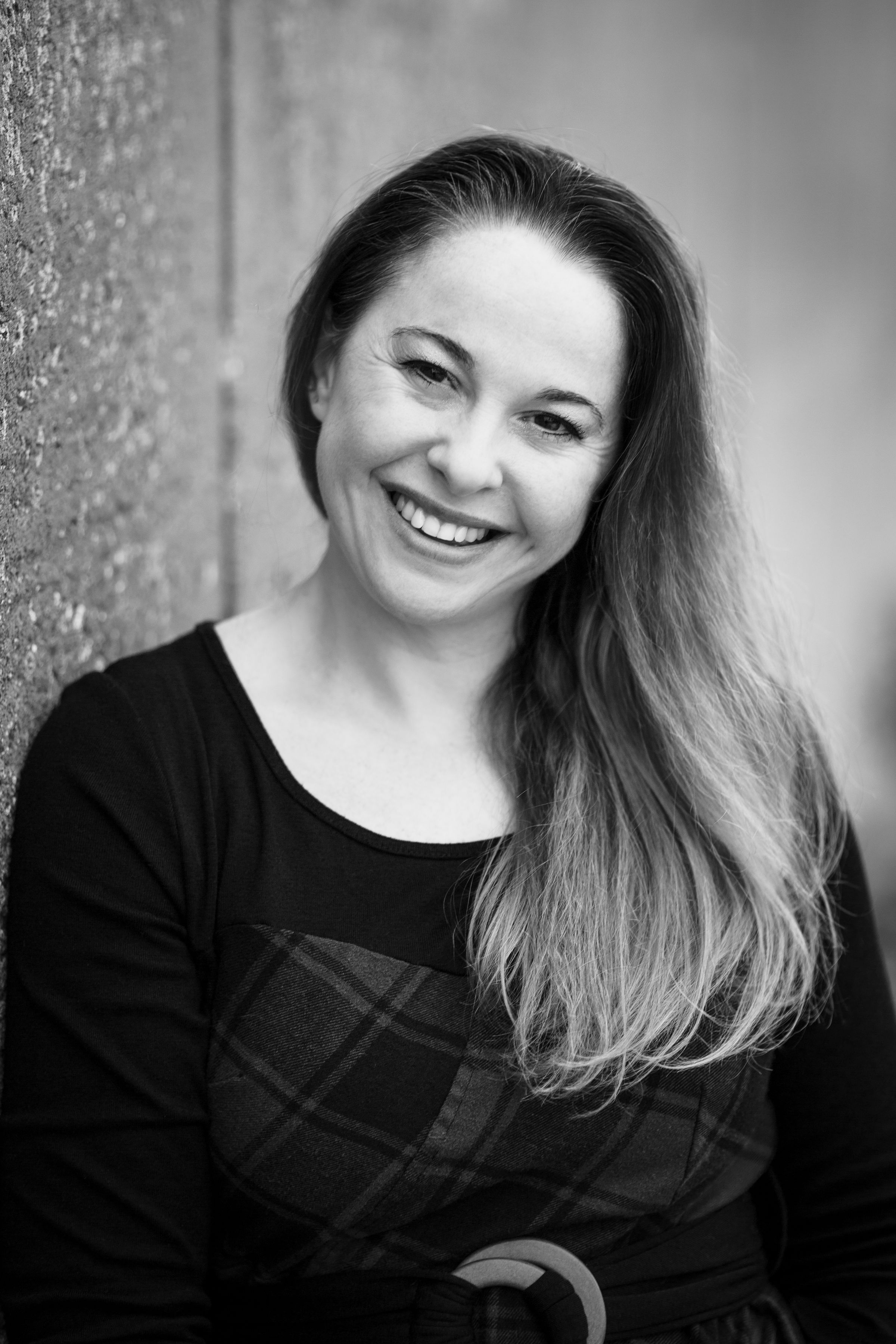 Black and white portrait of a smiling person leaning against a textured wall.