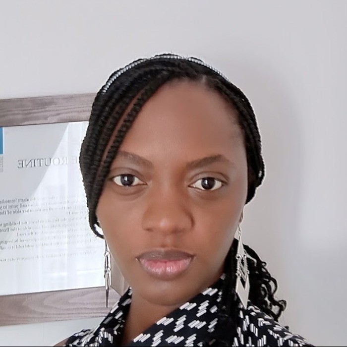 Close-up portrait of a person with braided hair and earrings, standing indoors.