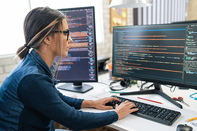 Woman working in front of computer monitors with software code