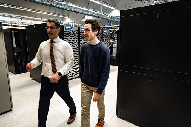Civil Engineering Faculty Two men walking through a data center lined with servers. One wears a white shirt and tie, the other a dark sweater. They appear focused and engaged.