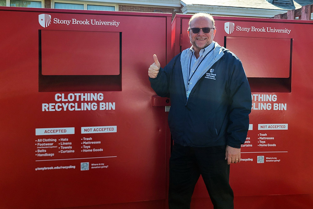 image of an employee standing in front of a red clothing donation bin