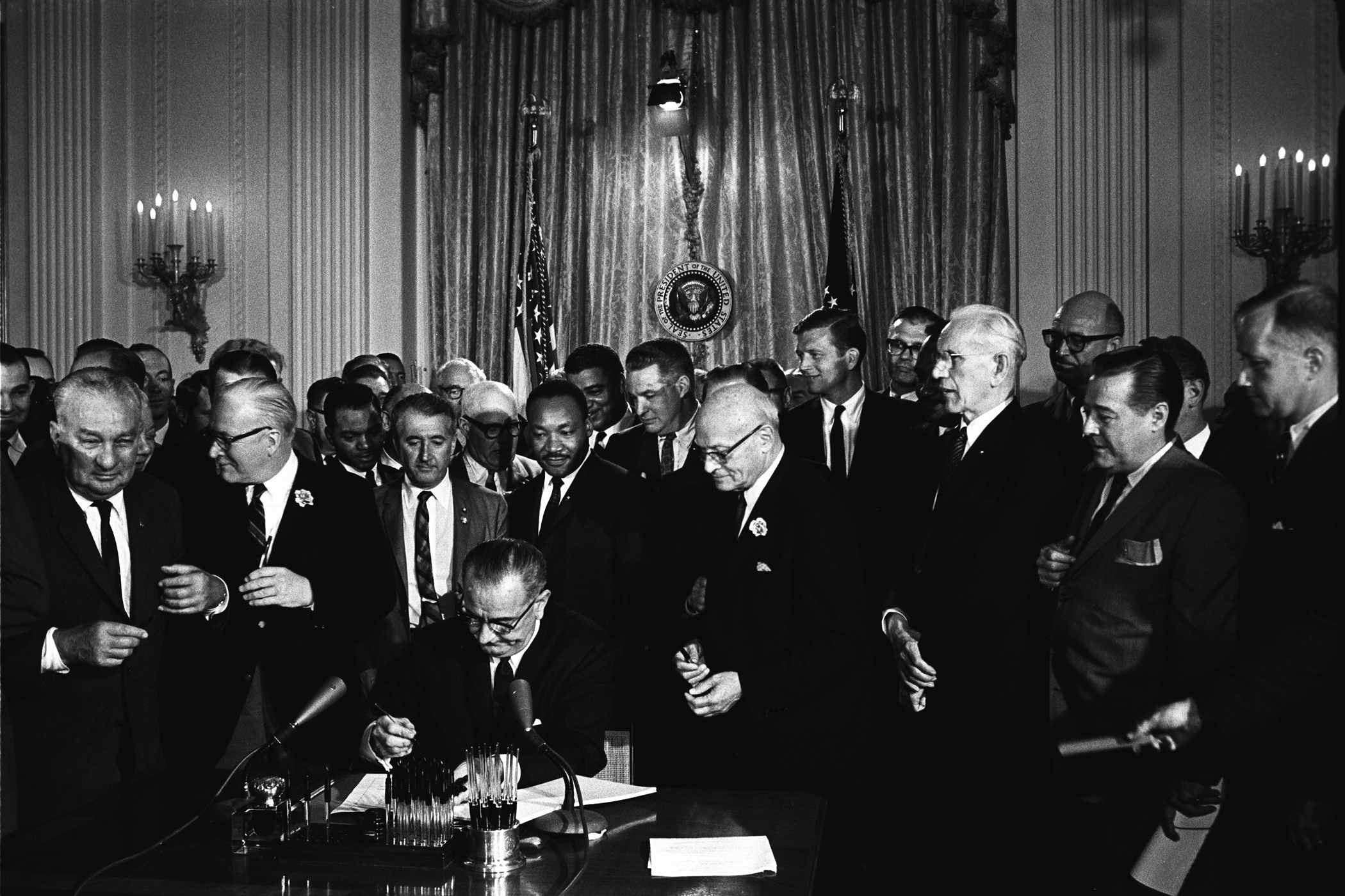 Lyndon johsnon signs the civil rights act of 1964 surrounded by onlookers including Martin Luther King