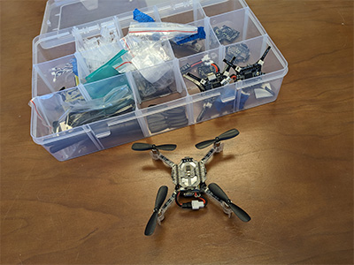 Micro quadcopter next to a box of parts