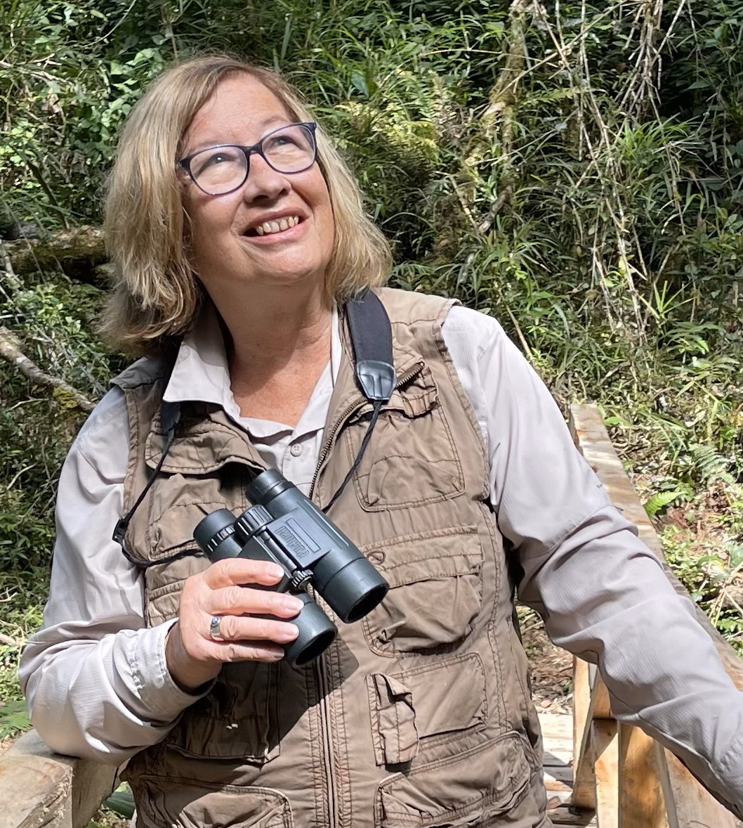 Pat Wright holds binoculars in a forest in Madagascar