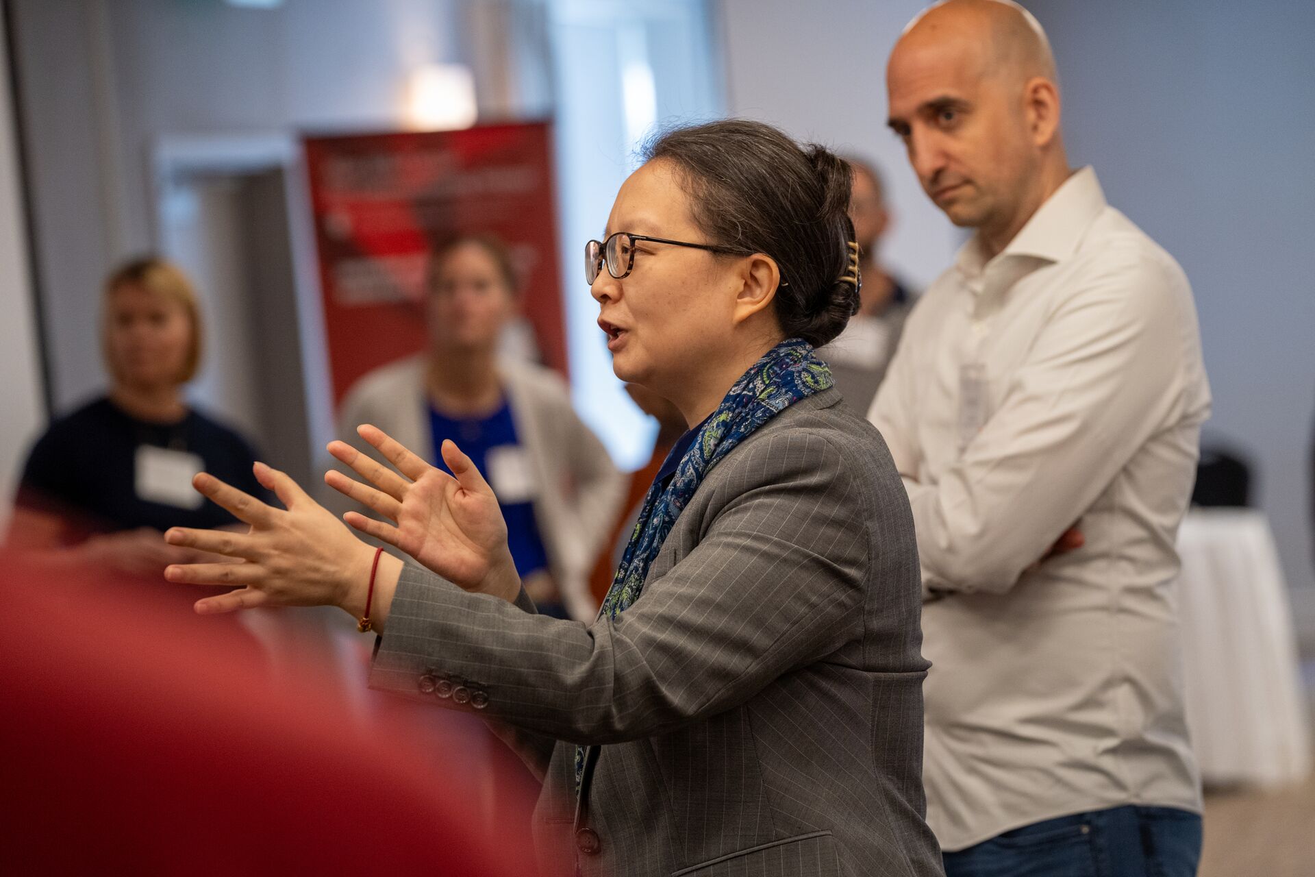 A person speaks to a group during a professional workshop while others listen in the background