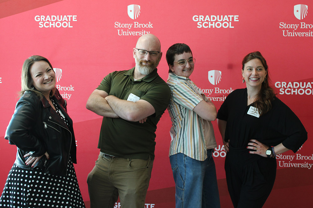 Four people posing and a graduate school steo and repeat in the background.